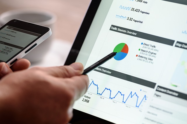 Hand holding pencil pointing to computer screen with graphs and charts