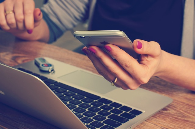 Woman's manicurred hand with wedding band holds calculator in front of laptop screen