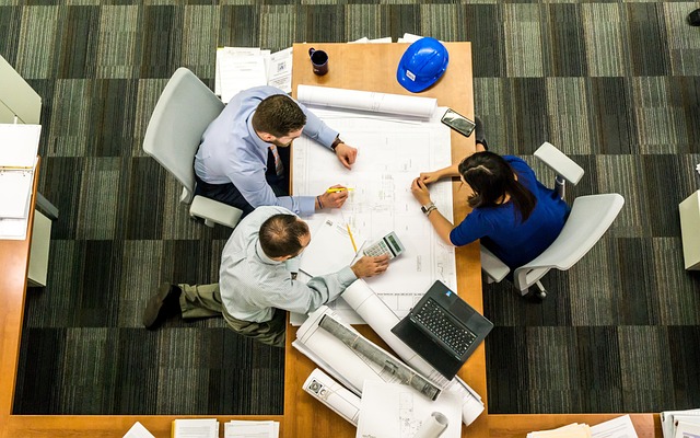 Birds view of a desk with papers surrounded by three people in a meeting