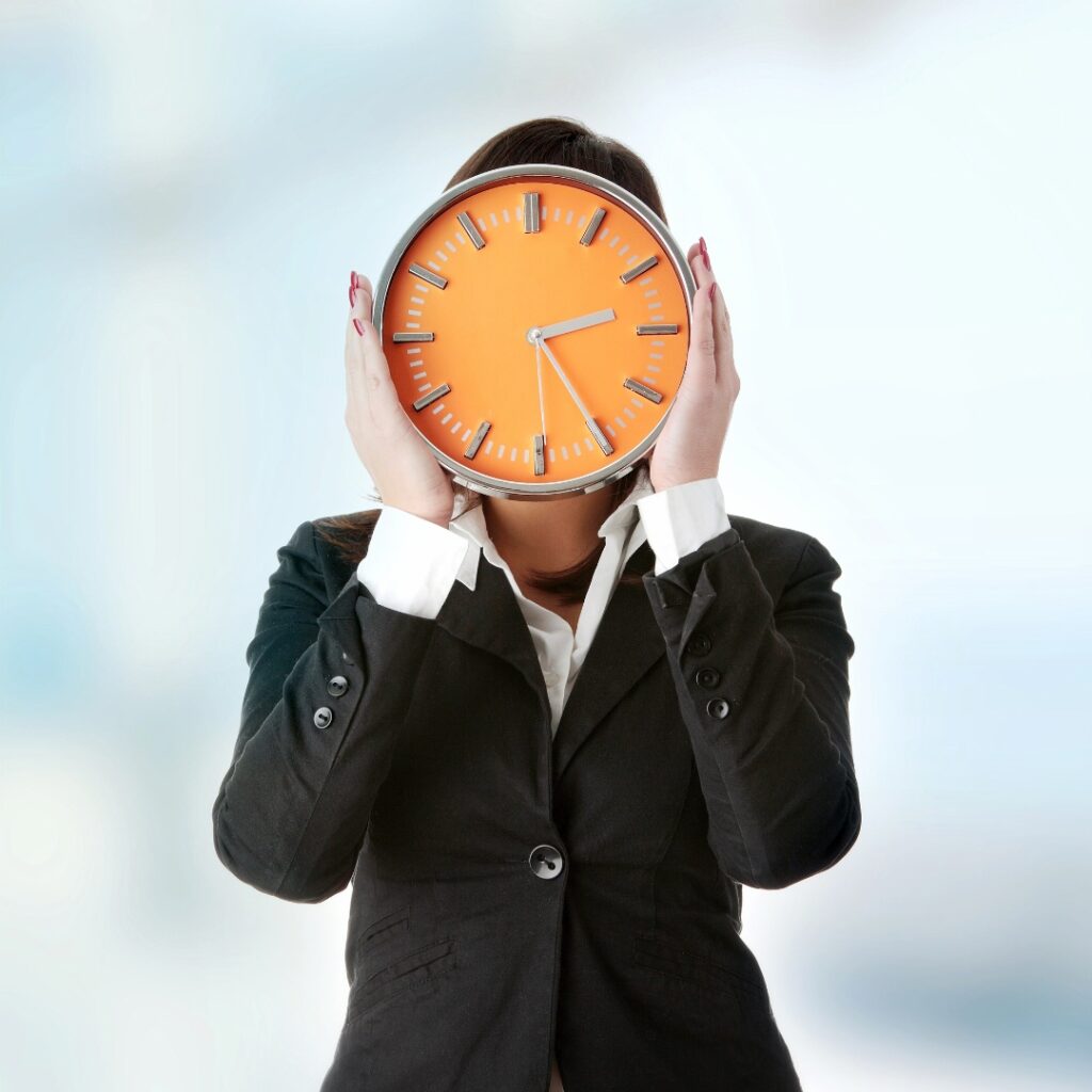Person in a business suit holding a clock in front of their face.