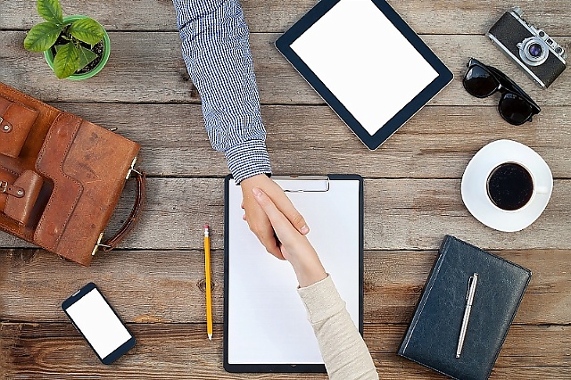 Handshake over a desk with office supplies.