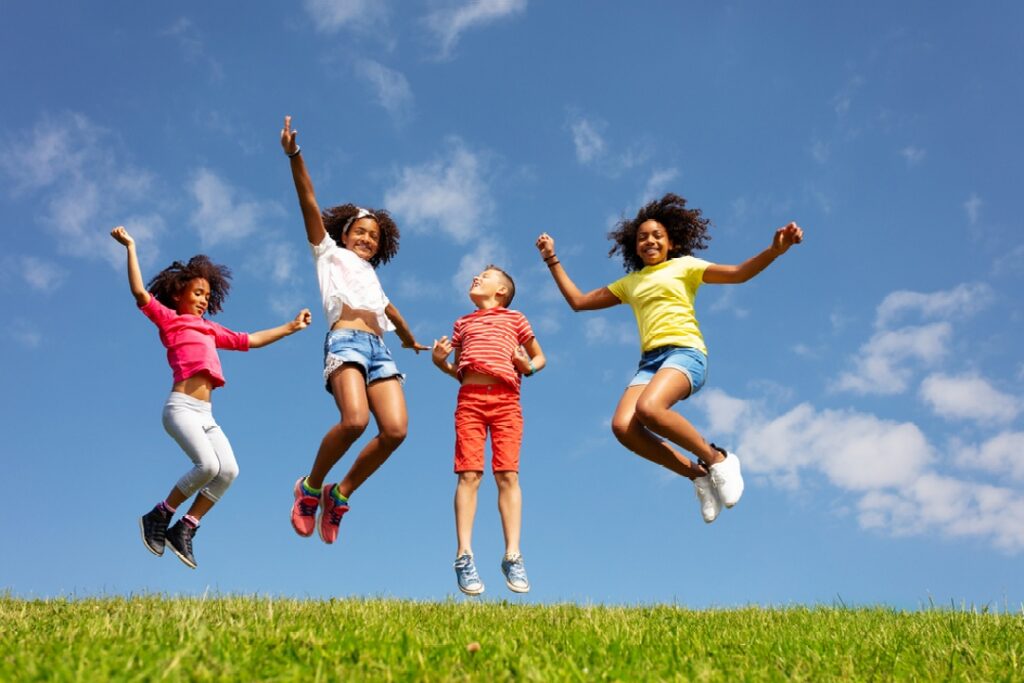 Four happy children jumping up in a field with big sky behind them.