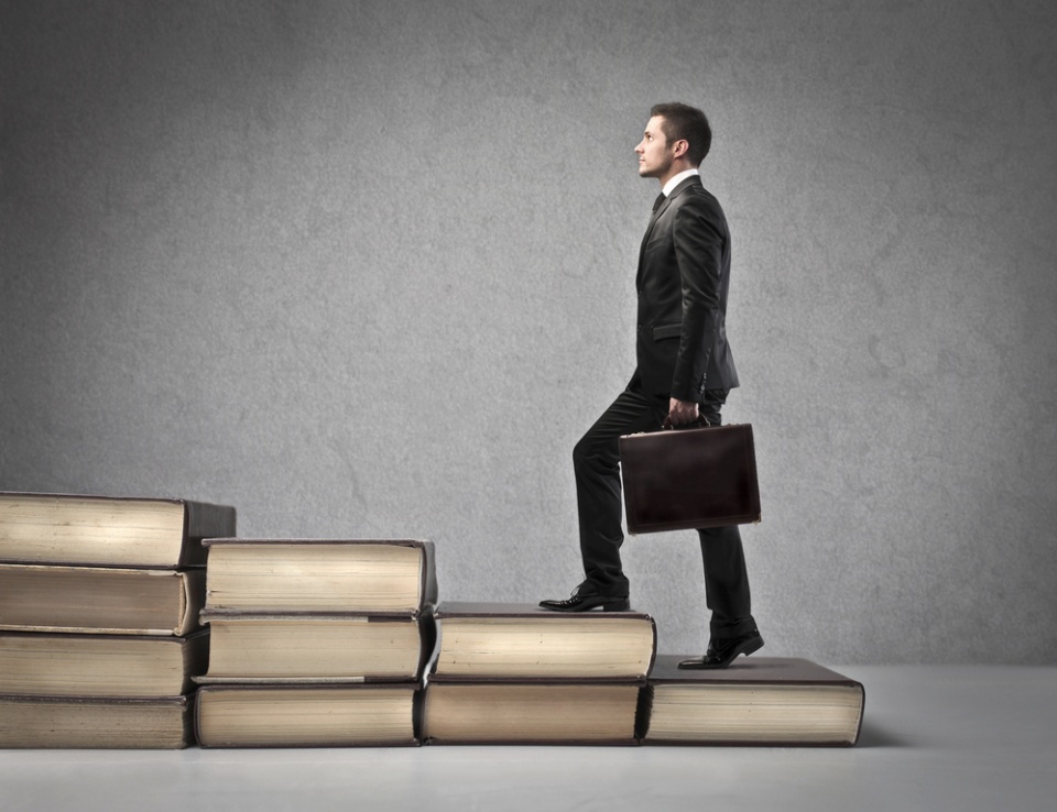 businessman holding briefcase climbing a staircase made of books