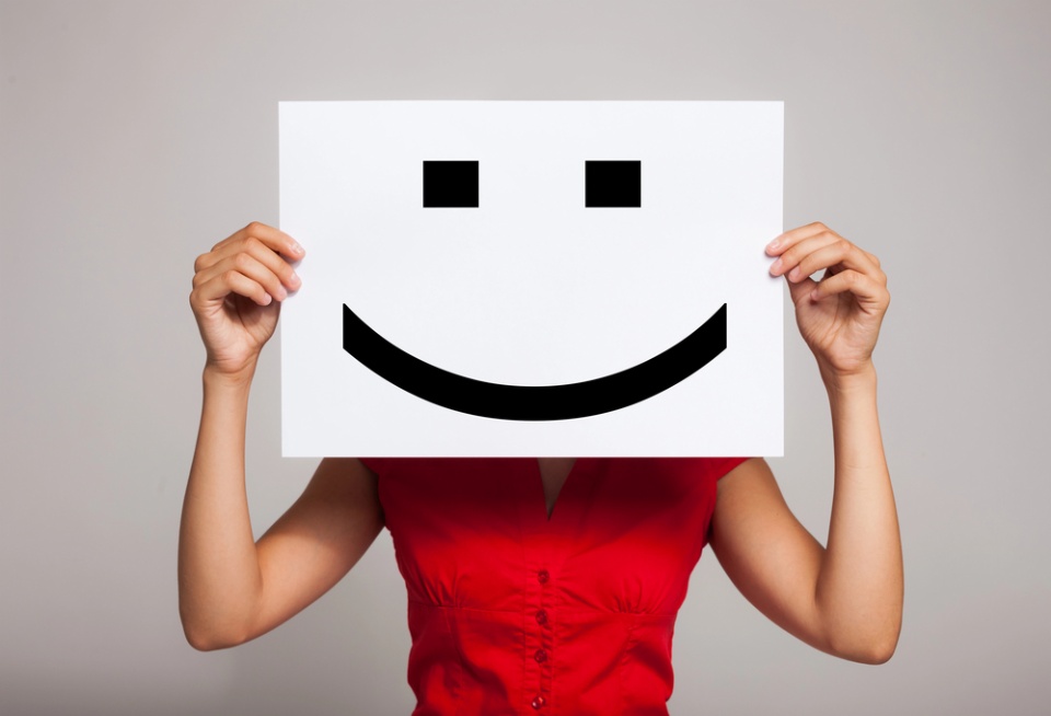 woman holding smiley face sign in front of her face