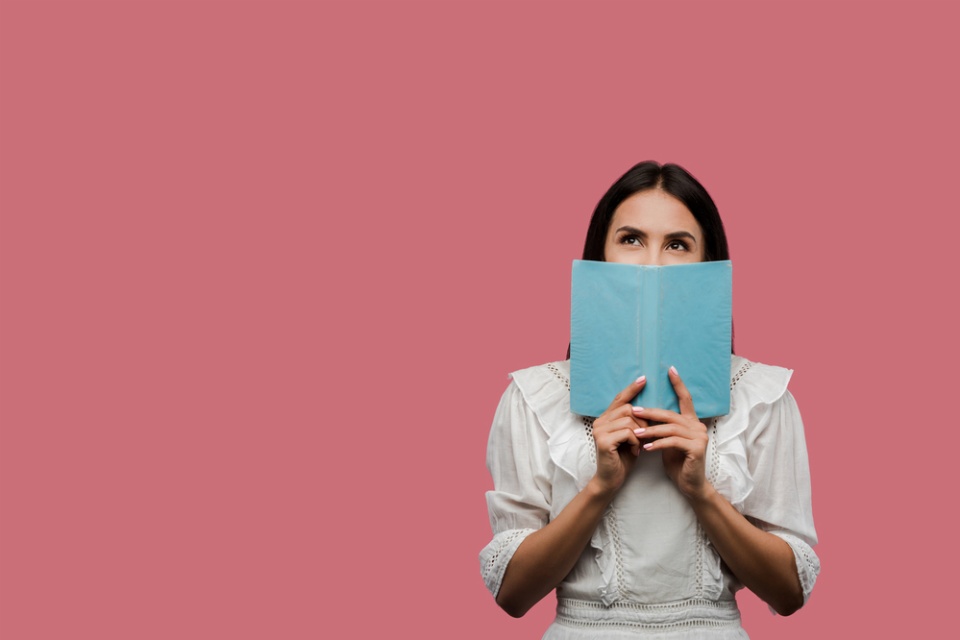 woman holding a book in front of her face, you can only see her smiling eyes