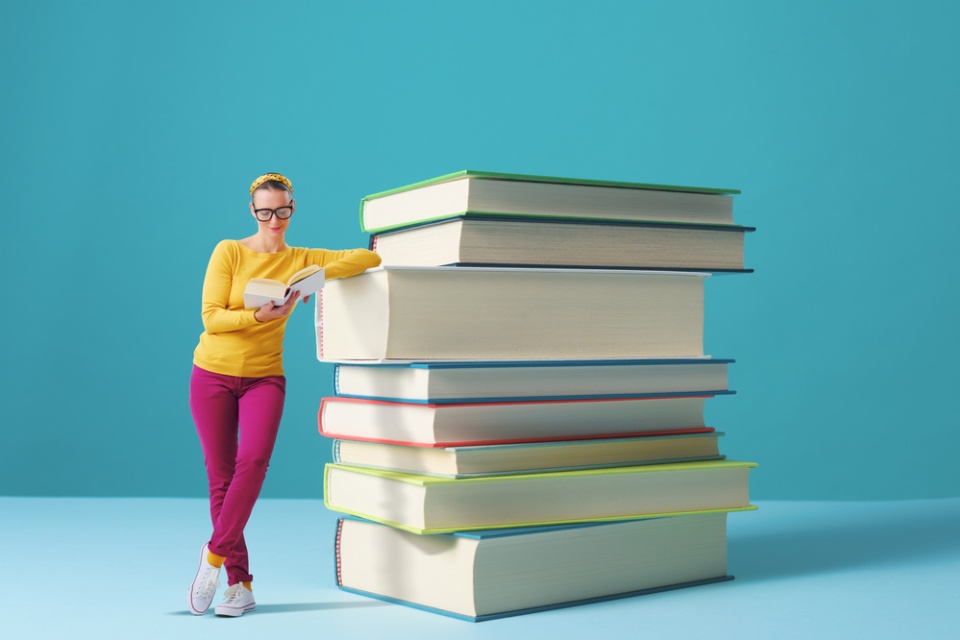 woman standing next to and leaning on a pile of giant books