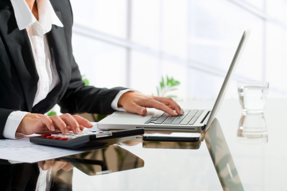 woman typing on laptop with one hand and using calculator with the other