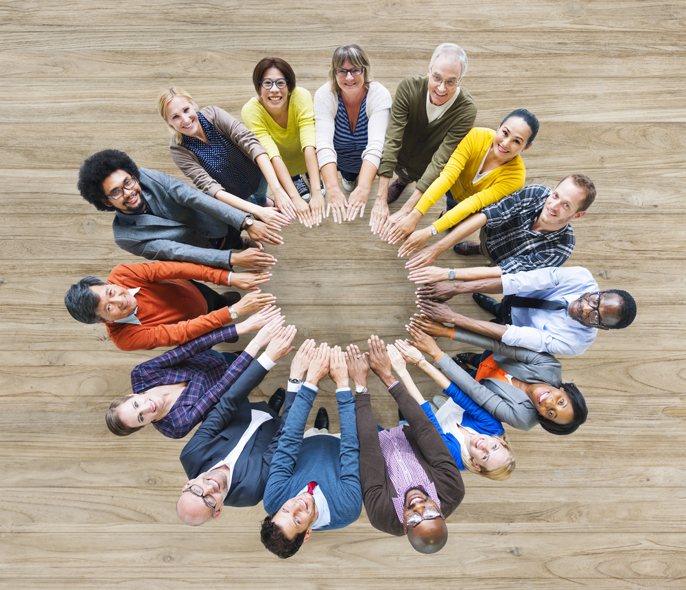 15 people standing in a circle, arms extended, looking up and smiling