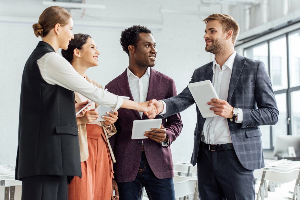 four people standing together and smiling; two shaking hands